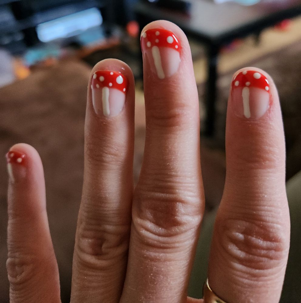 Close up on fingers; the nails are painted with red French tips with white dots, amd a white stripe down the center: it's a bunch of little mushrooms! 🍄