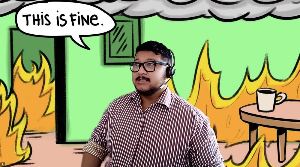 Man on videoconference webcam. In the background there is a cartoon office on fire, and the words "this is fine" in a speech bubble.