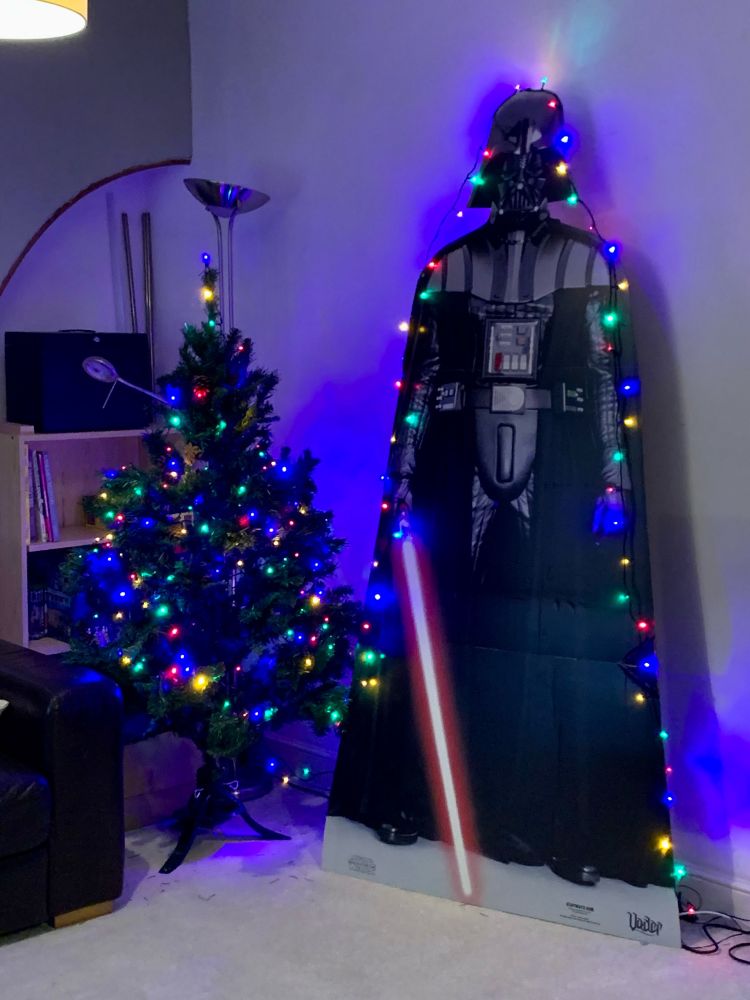 The Dark Lord of the Sith, outlined in multicoloured lights, towers next to a similarly bedecked small tree.