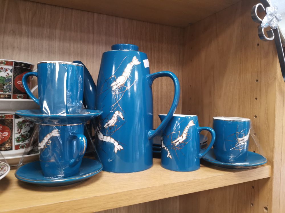 Espresso cups and a jug in blue with a large white king prawn on each piece.