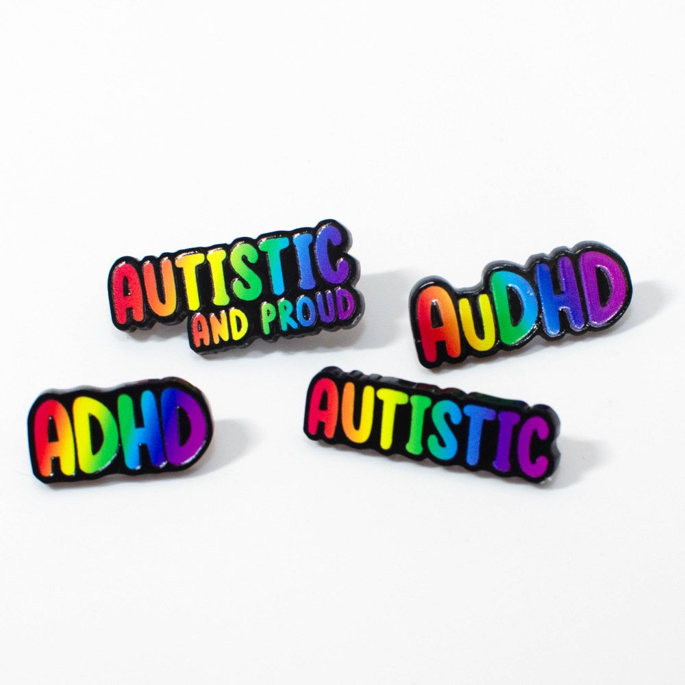 four black acrylic pins with rainbow writing. they says Autistic and proud, AuDHD, ADHD and Autistic