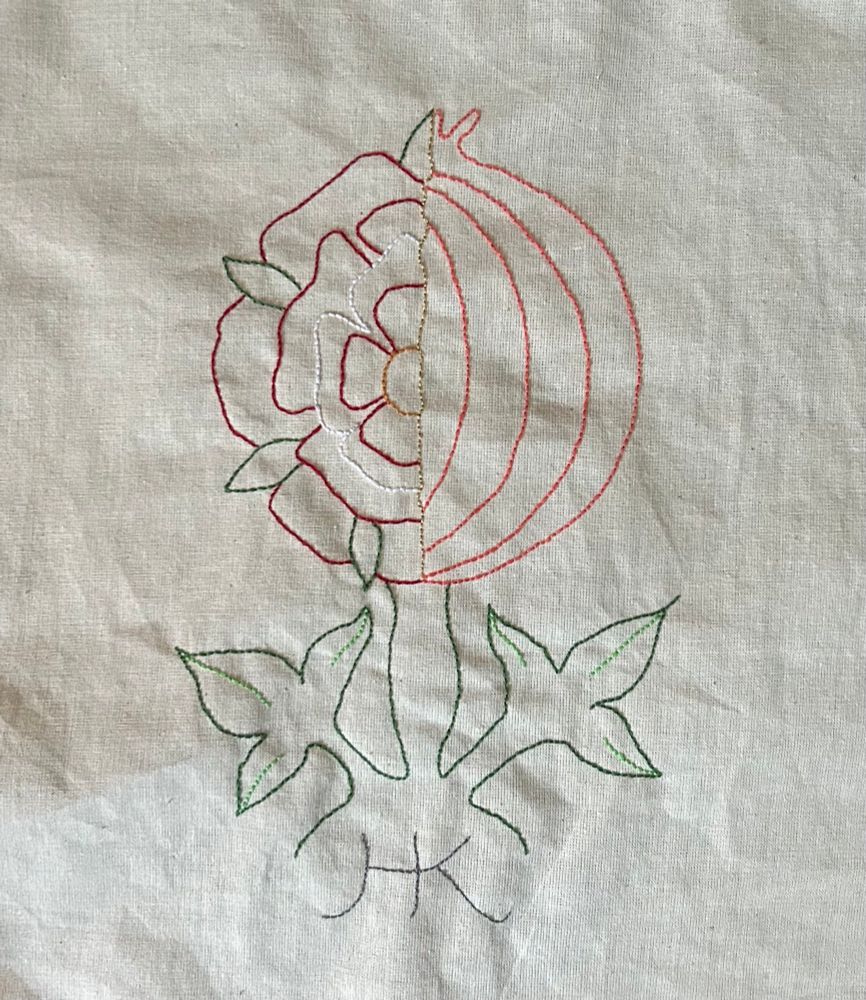 An embroidered piece of work showing the emblem of Katherine of Aragon - a Tudor Rose and a pomegranate, halved and joined. The initials H and K are stitched at the bottom. 