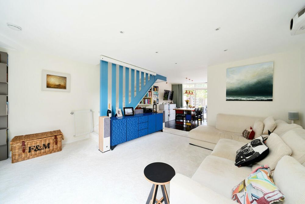 The downstairs of one of the paralellograms with the staircase hidden behind vertical planks of wood painted blue, and a blue sideboard in front of it.