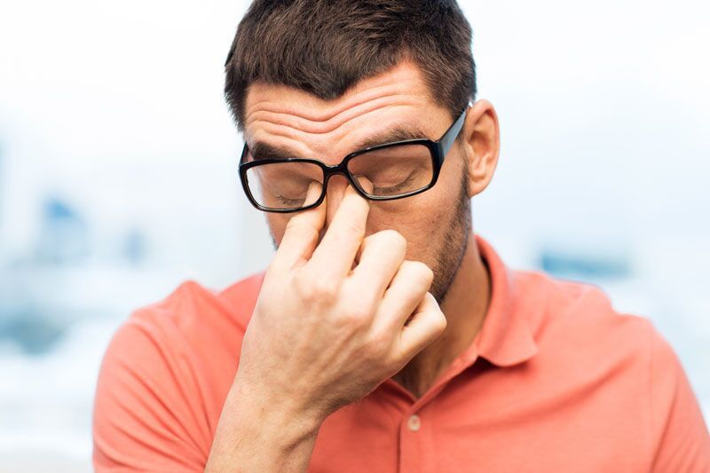 stock photo of a person pushing their glasses up so they can pinch the bridge of their nose in frustration