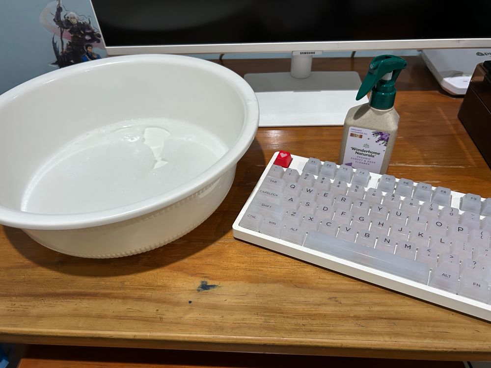 a white mechanical keyboard with translucent keycaps, a white basin of water, and a spraybottle of cleaner on my desk