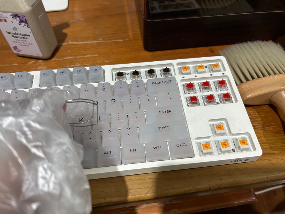 the keyboard with a few keycaps removed to show the switches; there is a keycap puller in my gloved hand 
