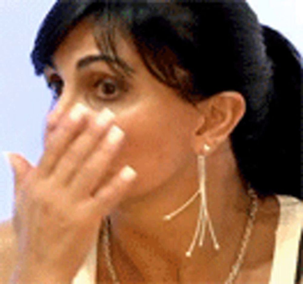 a woman is covering her mouth with her hand and wearing earrings