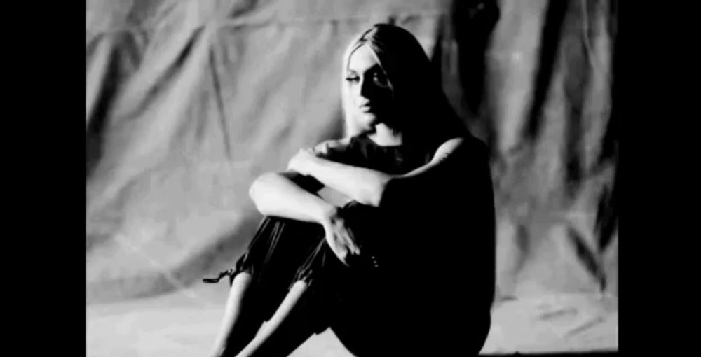 a black and white photo of a woman sitting down with her legs crossed .