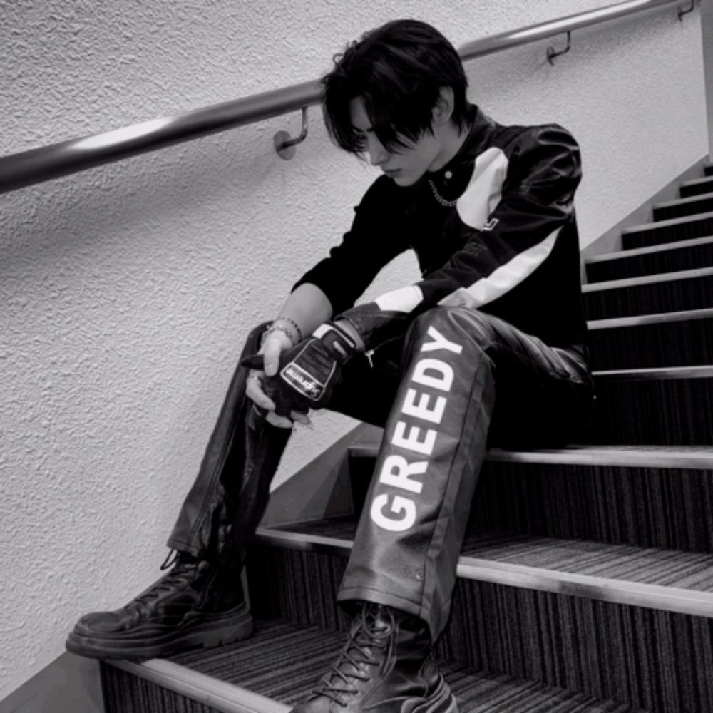 a black and white photo of a man sitting on stairs with greedy written on his pants