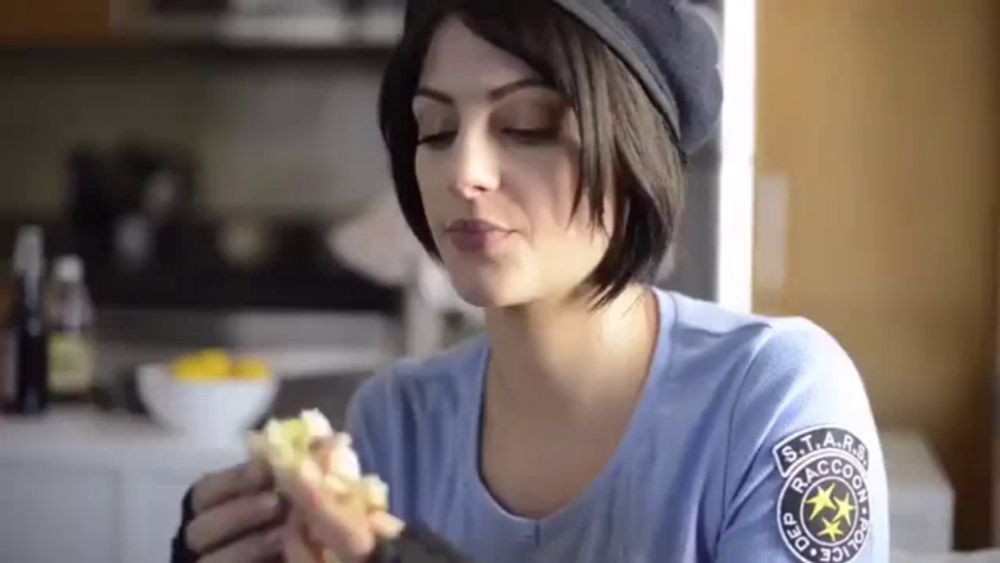 a woman is eating a sandwich in a kitchen .