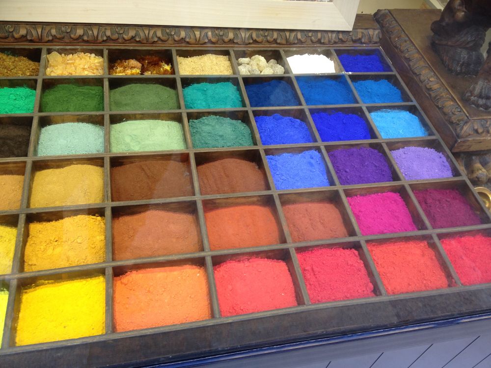 Eine Art Schubkasten aus Holz mit vielen Fächern, die prall gefüllt sind mit fein gemörserter Farbkreide in vielen leuchtend bunten Farben.