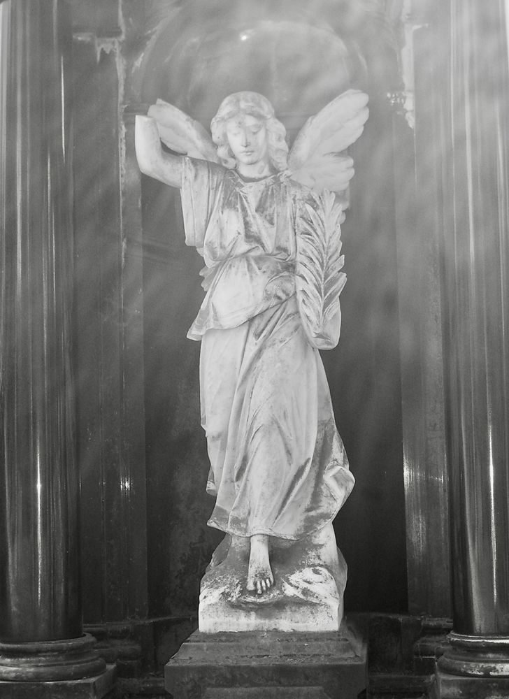 Schwarz-weiß Bild die Statue eines weißen Engels in einem schwarzen Tempel – ein Grabmal.