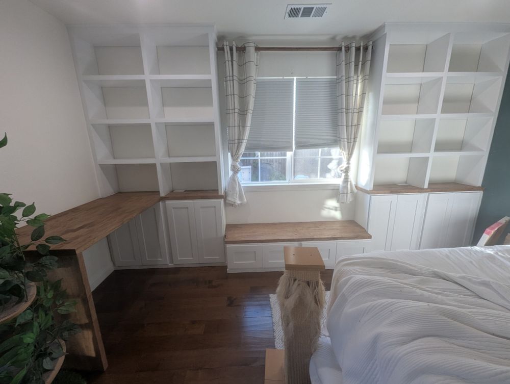 Wide angle photo of built in shelves and cabinets with an L shaped desk