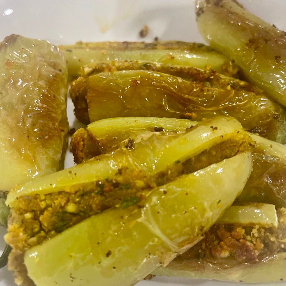 These light green peppers have been slit and generously filled with a spiced, crumbly mixture made from ground lentils, nuts, and aromatic Indian spices. Their slightly wrinkled, glossy surface hints at gentle sautéing, a classic technique in Indian kitchens to deepen flavor. This dish beautifully reflects the tradition of stuffing vegetables to create rich, savory bites that pair well with roti or rice.