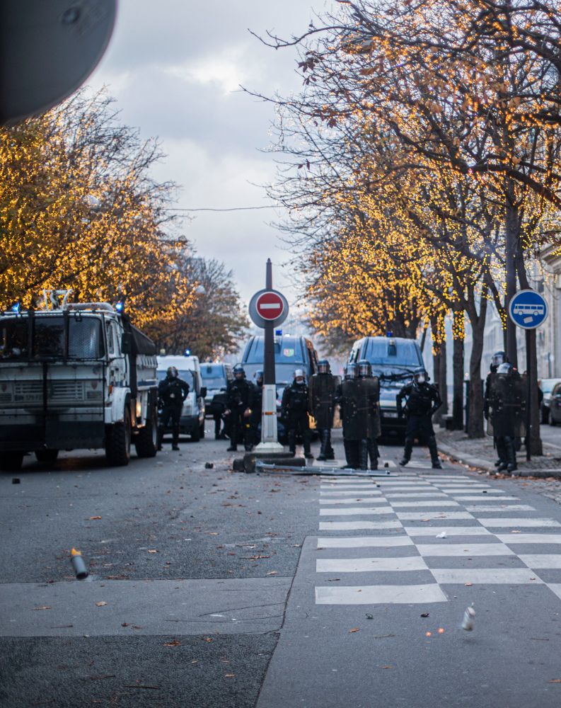 Une grenade offensive lancée par une ligne de gendarmerie mobile sous des arbres illuminés par des décoration de noël s'approche pour bientôt exploser aux pieds de la photographe