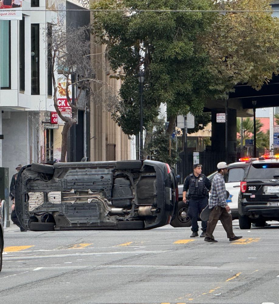 a cop standing next to a car on its side (Duboce & Valencia in SF)
