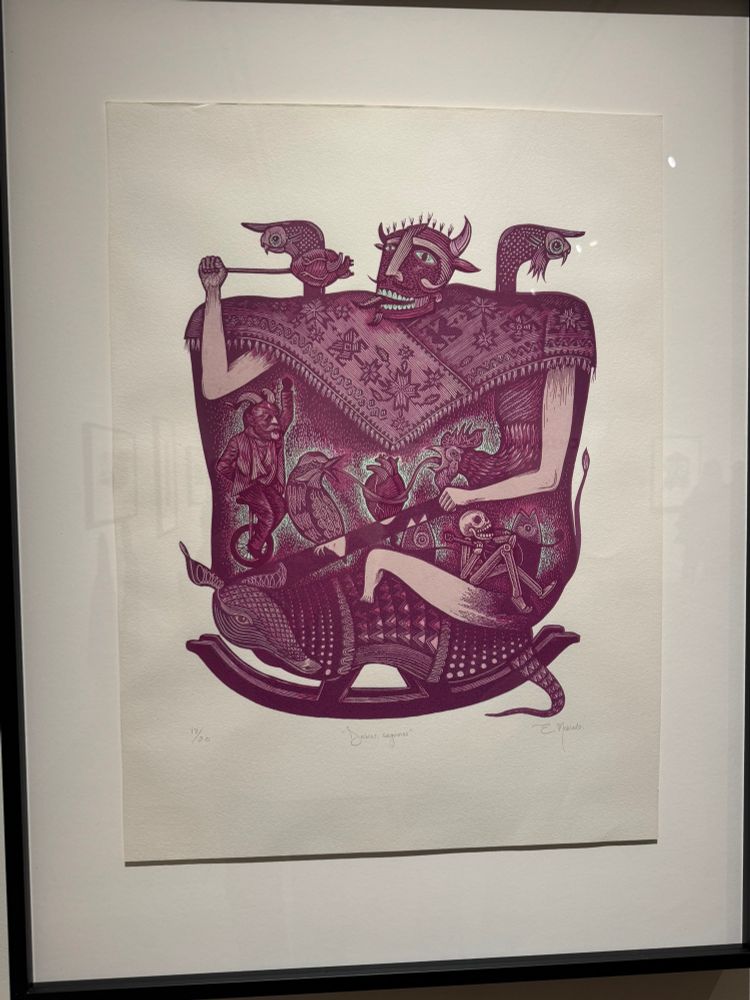 “Diablos, seguimos,” Eduardo Robledo, 2020. A linocut print in shades of plummy, pinky purples with robin’s egg blue or maybe seafoam highlights. A large, rectangular figure with horns draped in an ornate fabric, from which protrudes a slim tail. Fishes emerge from his shoulders. He points a heart impaled on a stick towards his mouth, pointed tongue reaching to meet it. Within or on top of his torso: a songbird and a chicken squawk their tongues at each other around another, central heart; a figure in a devilish mask rides a unicycle; a skeleton strums a guitar, song curling from his mouth; also, more fish. The rectangular figure rides an armadillo on rockers, like a child’s toy horse.