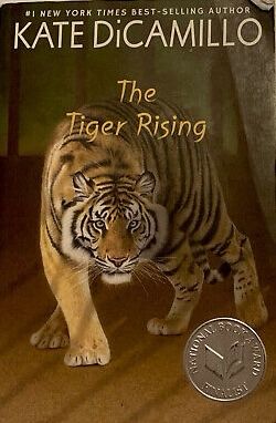 Book cover of The Tiger Rising by Kate DiCamillo, #1 New York Times Best Selling Author. There is a Tiger encompassing the whole cover, prowling aggressively toward the reader  