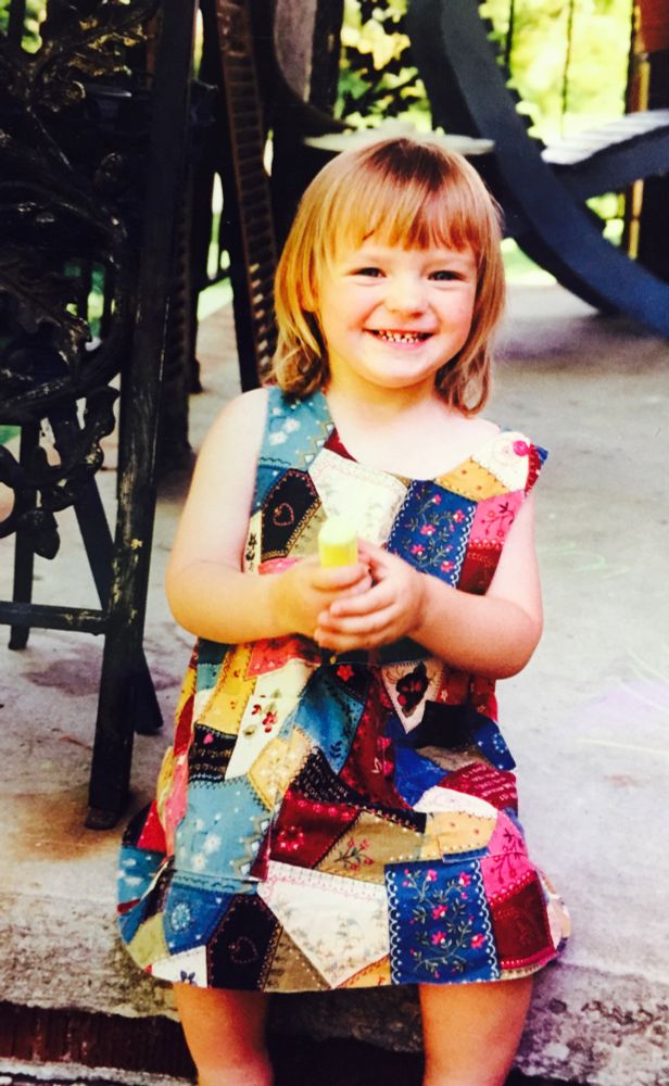 Toddler photo of me on the porch in a patchwork dress doing a big grin
