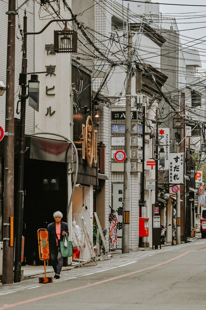 Vue d'une rue commerçante de kyoto, mettant en avant les poteaux électriques typiques du Japon et une personne marchant sur le trottoir