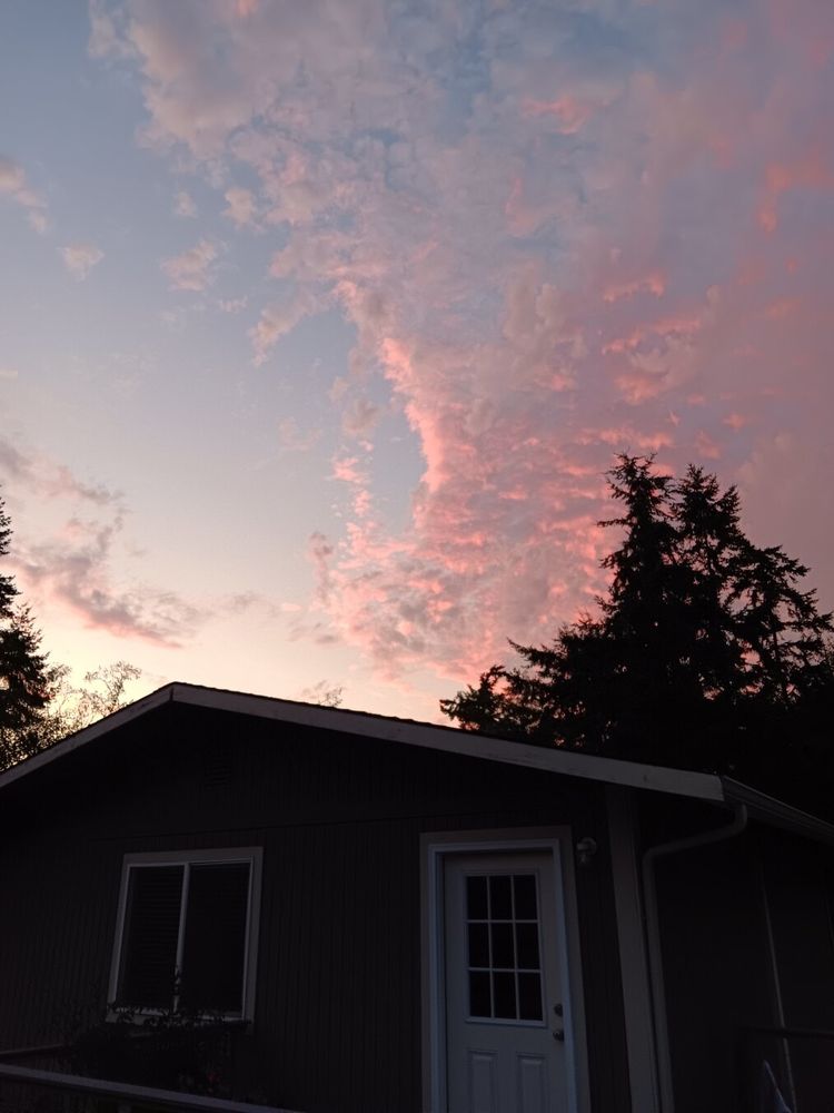A swath of Ripley clouds ranges up the right side of the image. They are lit up in pinks and purples from the sunset, contrasting with the Shaded blue of the left side of the sky. A small building is silhouetted in Black at the bottom of the image