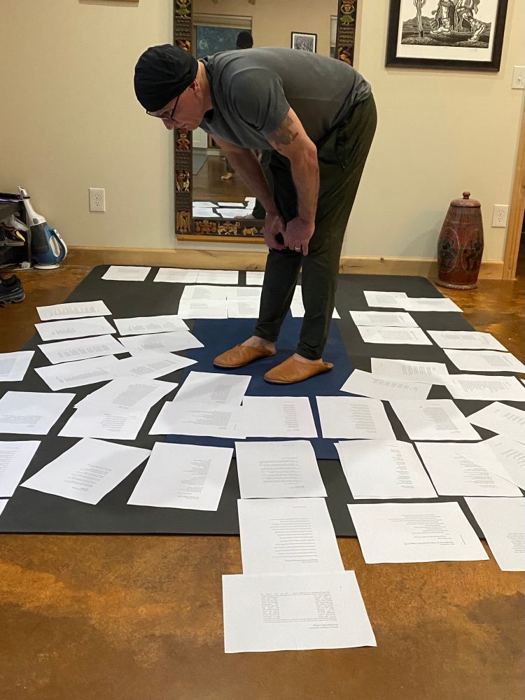 Man standing on a large yoga mat bent to examine papers spread around him