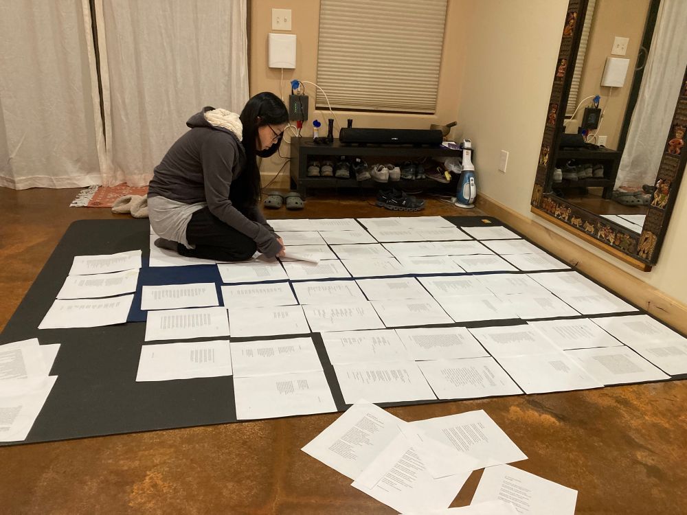 Woman sitting on a very large yoga mat looking at papers spread over it