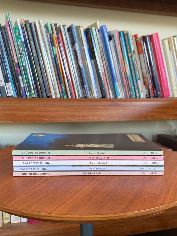 Shō issues 3 through 7 stacked on a small round table in front of a long wooden bookcase