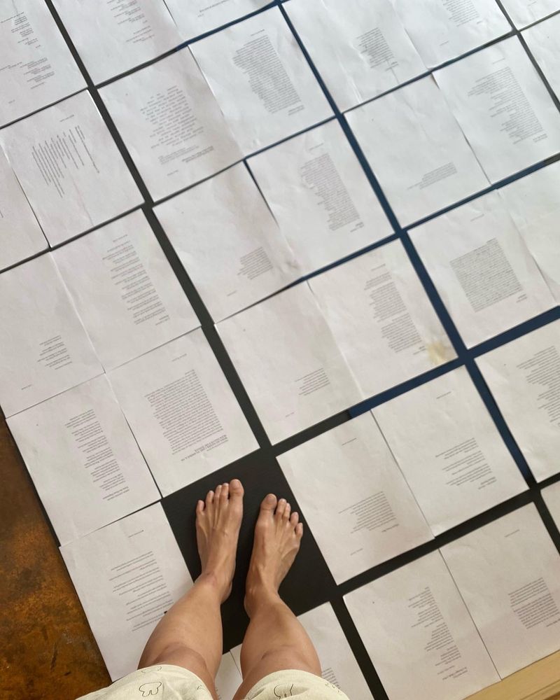 Looking down. Two legs and feet on a yoga mat with printed poems spread across it