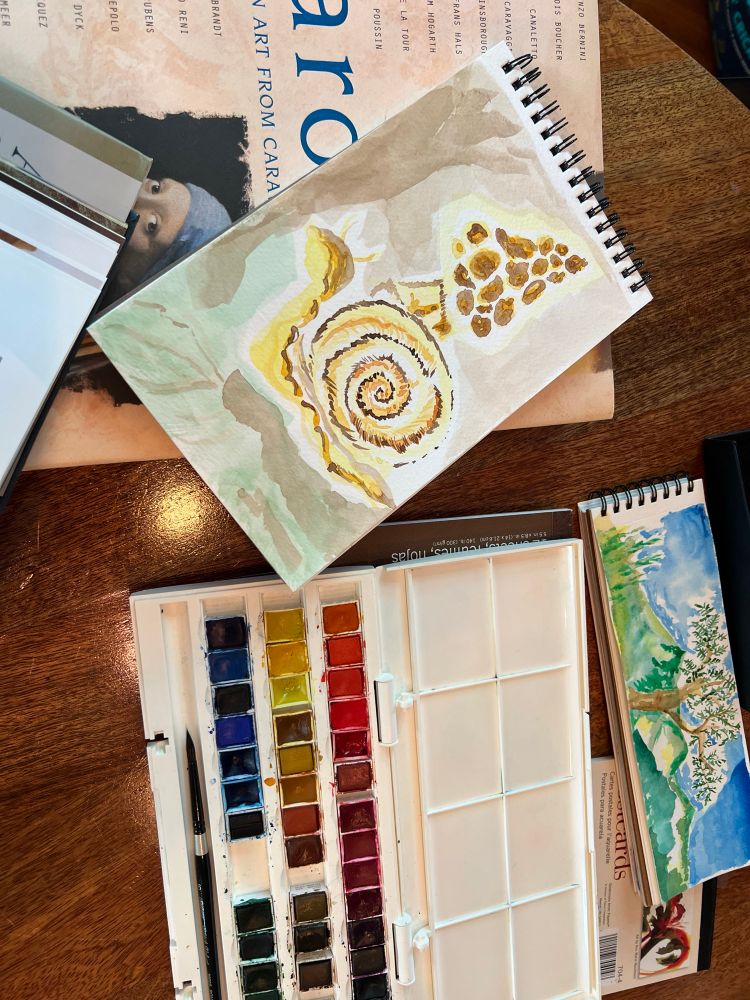A watercolor sketch of a snail and a morel mushroom along side a colorful box of watercolor paints; a small landscape sits above