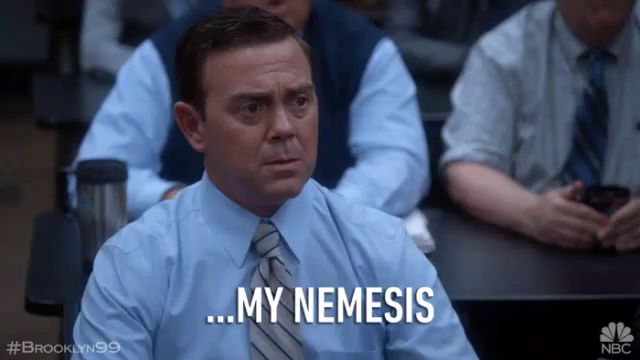 a man in a blue shirt and tie is sitting in a classroom and says " my nemesis "