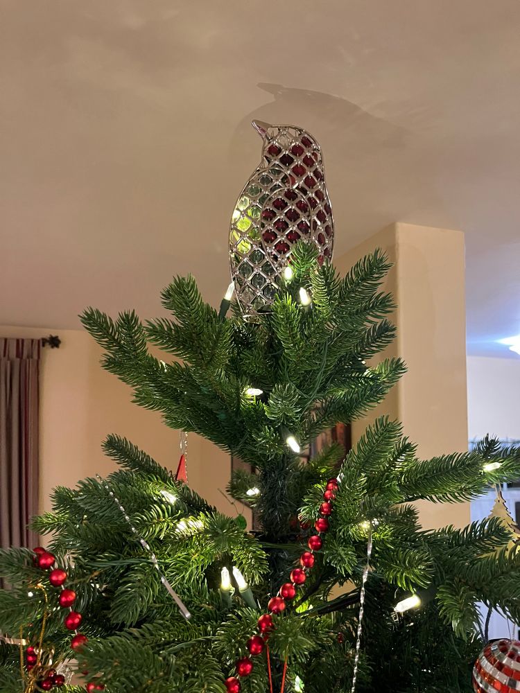 Metal and ruby red crystal penguin tree topper on top of an artificial Christmas tree