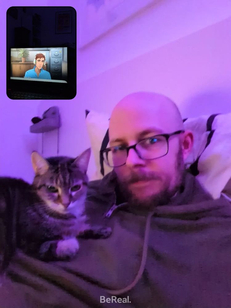 BeReal en que se ve a una persona estirada en la cama con un gato encima. En la otra foto se ve una pantalla de ordenador con un personaje cartoon. 
