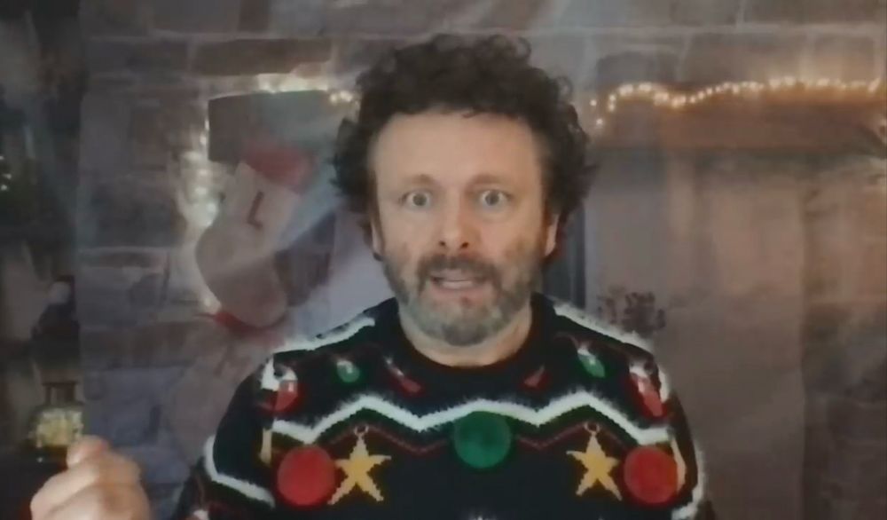 Michael Sheen from s3 of Staged in a Christmas sweater and has darker than usual hair