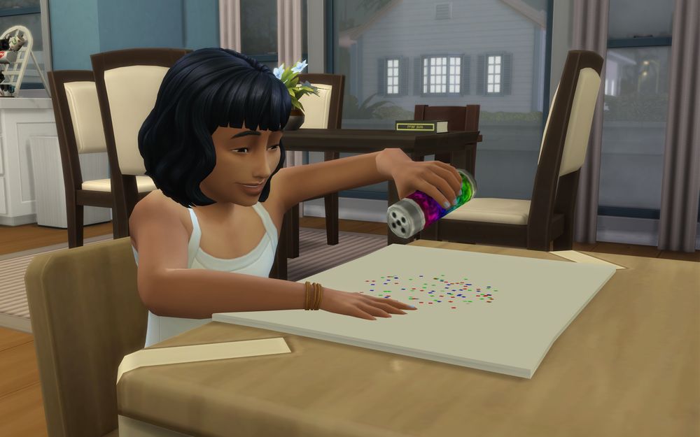 Tasha is sitting at her activity table and throws glitter on a piece of paper.