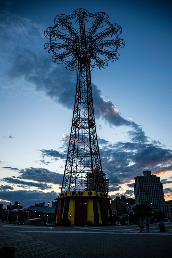 the iconic Coney Island parachute drop with dramatic clouds in the darkening sky behind it. 