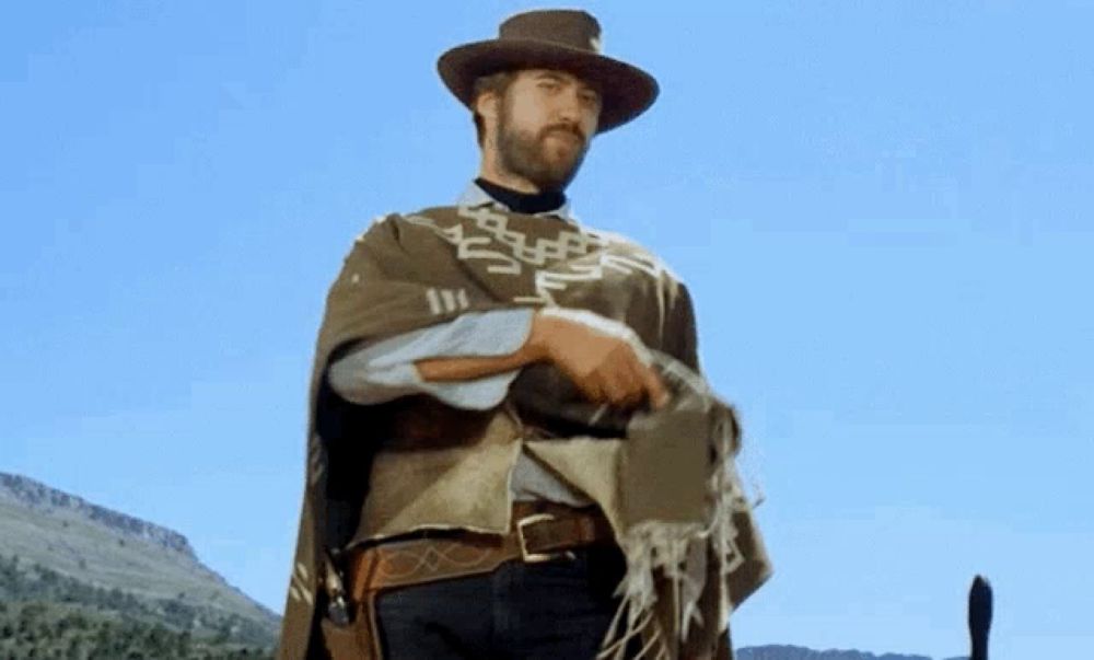 a man in a hat and poncho is standing in the desert .