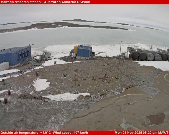 A view of the Mawson research station, a few small buildings and equipment scattered across rocky terrain.