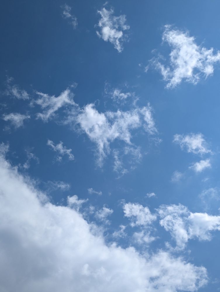 Blue sky with thick cloud at bottom left and various smaller clouds scattered above it. The sun is outside of the frame on the right.