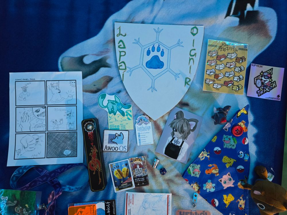 L to R:Comic Panel pass, dice set from Challenge; Glaceon sticker and Awoo OS patch from ArGiBi; made a crest for a shield from the Meadow #IcePaw with my name in uncial script; art from @rendelmouse; nigiri and furry trash sticker from Supykun; Zorua and Tom Nook plush from TTFN panel traded for Nomad pins; Pokémon bandana from Blue Canary Gallery; D20 from VixesRin; 10mm socket from Frostbyte Foxcoon; Royalty playing card won by rolling an 18 (definitely checking out their card game)