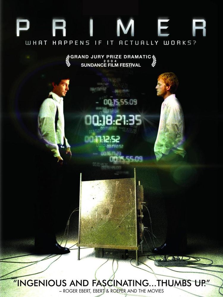 The poster for the movie Primer (2004). It features the two main characters Aaron and Abe, facing each other on opposite sides of what looks like a metal cube with various wires plugged into it. At the bottom is a quote by Roger Ebert: "Ingenious and fascinating...thumbs up"