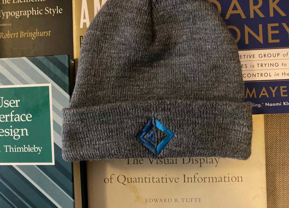 Grey beanie hat with embroidered #fsharp logo in blue, surrounded by pretentious book covers.