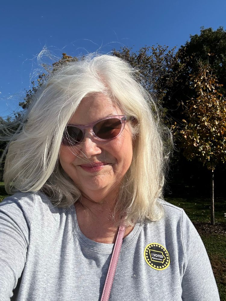 A white-haired woman in a grey shirt with an I Voted sticker on