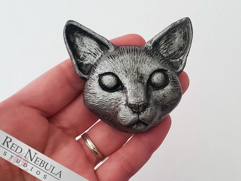 A hand holding up a resin-cast cat magnet, painted to look like it was made of silver.