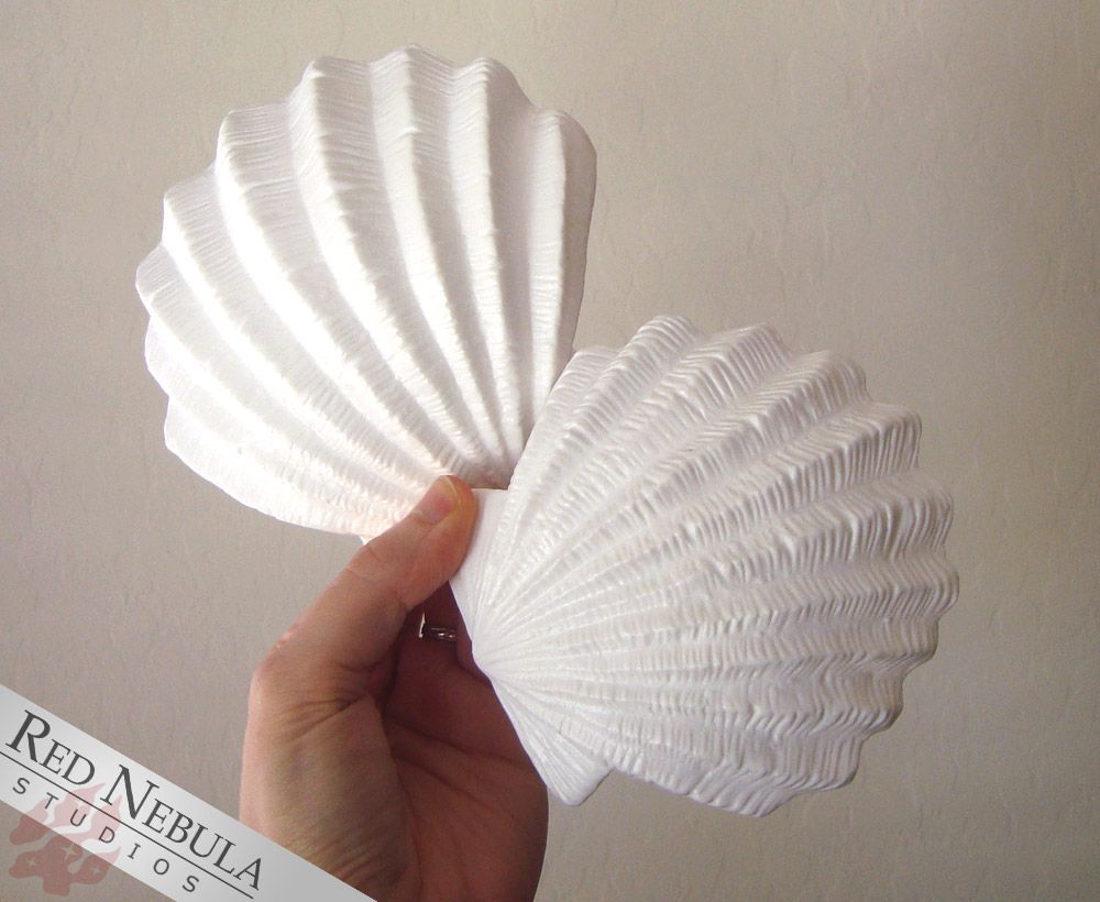 A hand holding up a pair of white resin cast seashells.