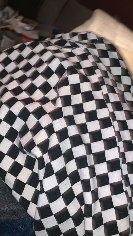 Hoodie auf 1 Couch geworfen. Der hoodie is schwarz weiß kariert ca 1,5 cm Karo. Die Umrisse von Ärmel, Kapuze und Rest verschwimmen im Muster. 