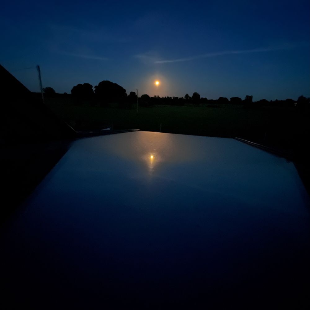 Picture taken of the night sky with the moon reflecting off a tilted open rooftop window.