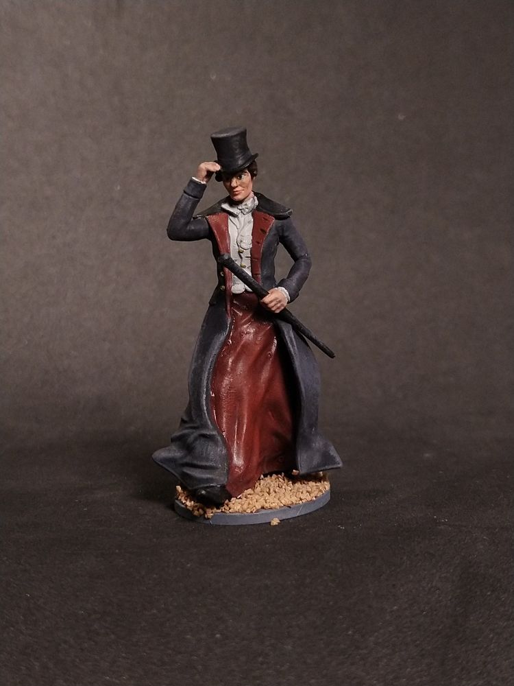 Das Bild zeigt eine kleine Figur, die einen eleganten, schwarzen Mantel und einen schwarzen Hüte trägt. Die Figur steht auf einem runden, braunen Basis, der an Erde erinnert. Sie hält einen Stock in der rechten Hand und hat eine klassische, formelle Haltung. Der Mantel ist lang und reicht bis zu den Knöcheln, und die Figur hat eine schlanke Silhouette. Der Hintergrund ist ein einfacher, dunkler Farbton, der die Figur hervorhebt.