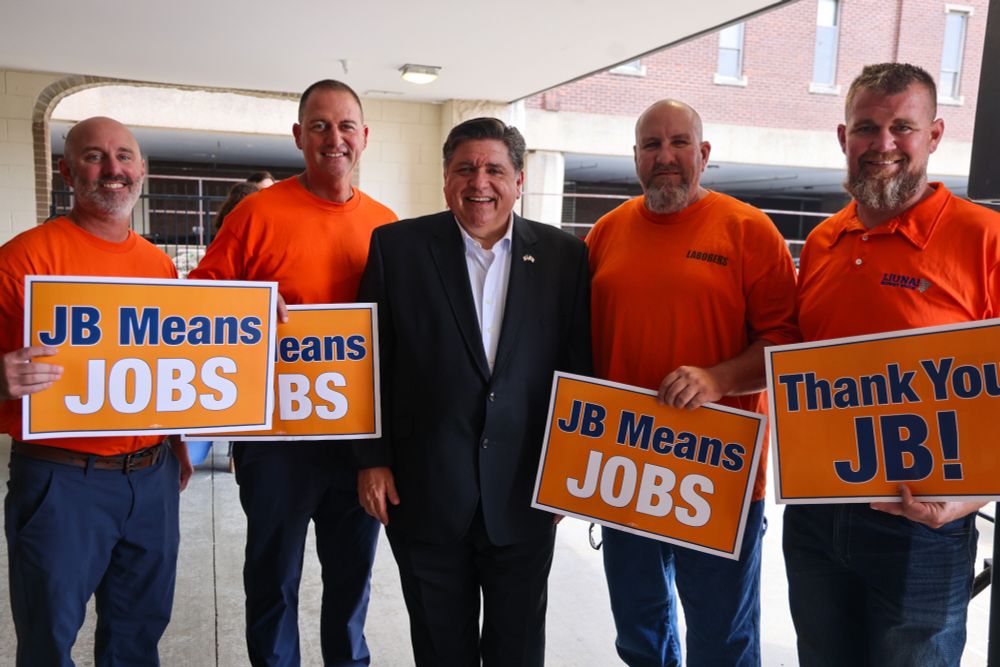 Governor Pritzker stands with constituents holding signs that read 'JB Means Job' and 'Thank you JB!'
