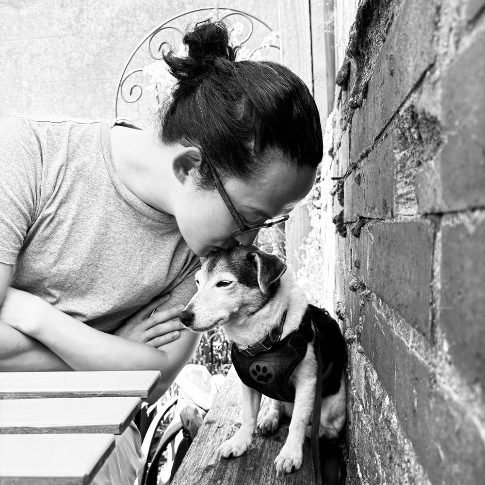 A black and white photo of a Jack Russell being kissed on the top of her head as she thinks about her favourite dinner: pollo. 